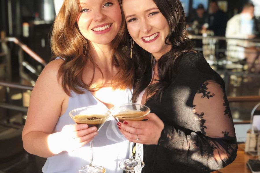 Two friends clinking espresso martinis on a sunlit bar terrace