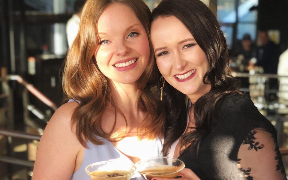 Two friends clinking espresso martinis on a sunlit bar terrace