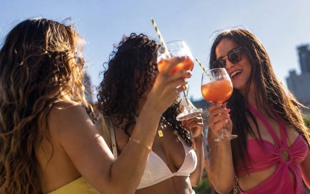 Friends toasting orange cocktails on a sunny rooftop