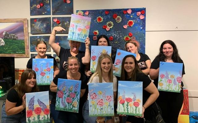 A hens group holding up their floral paintings at a paint and sip class