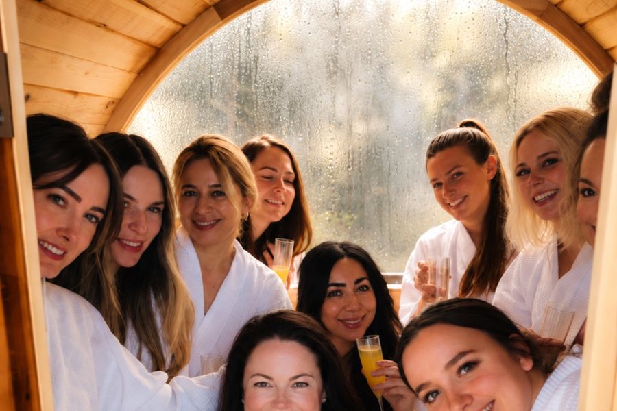 A hens group in white robes squeezed into a barrel sauna