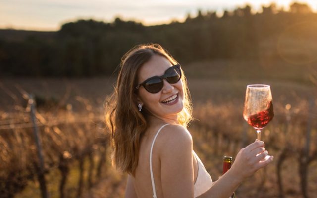A smiling hen with a glass of rose in a vineyard at sunset