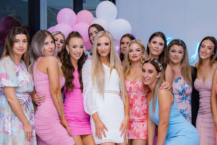 A hens group in pastel dresses posing together in front of pink and white balloons