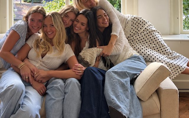 Six friends piled onto a couch, laughing