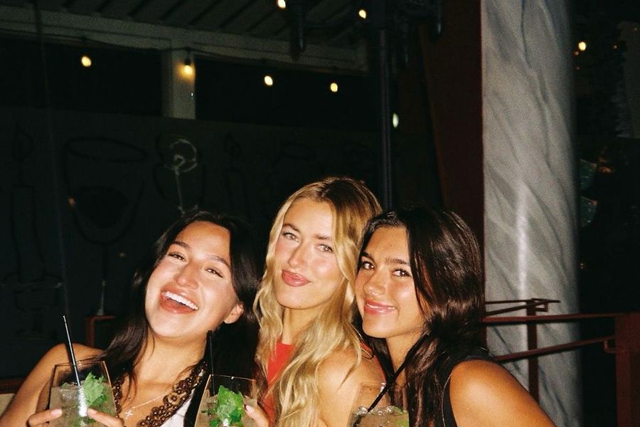 Three friends with cocktails under string lights at a bar