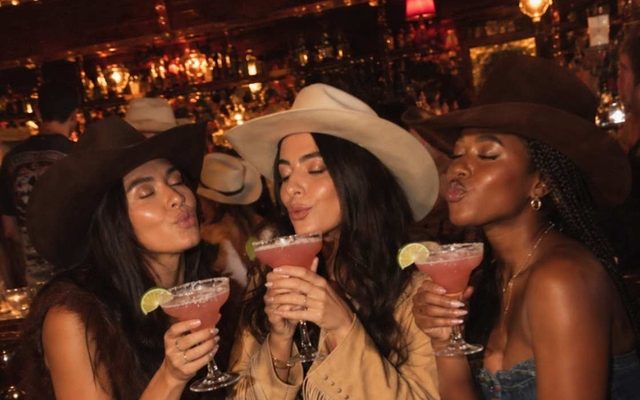 Three friends in cowboy hats sipping margaritas on a night out