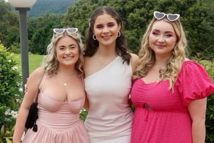 Three friends in pink dresses and heart sunglasses on a garden lawn with hills behind