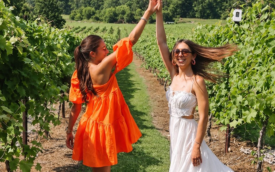 Two friends dancing hand in hand between the vines on a winery tour