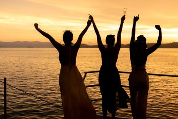Four friends with their arms up on the water at sunset