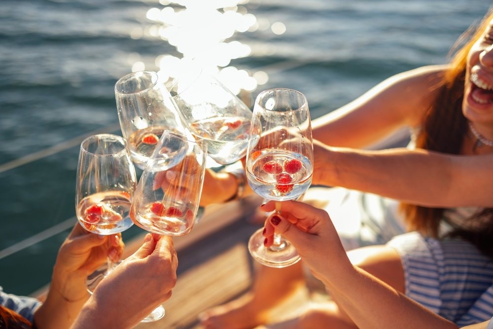 Hands raising glasses of rose bubbles over sunlit water