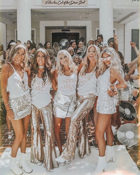 A group of friends in white and silver sequin flares posing outside a white house
