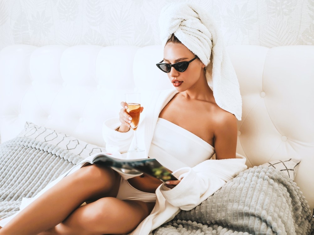 A woman in a white robe and towel turban relaxing with a cocktail