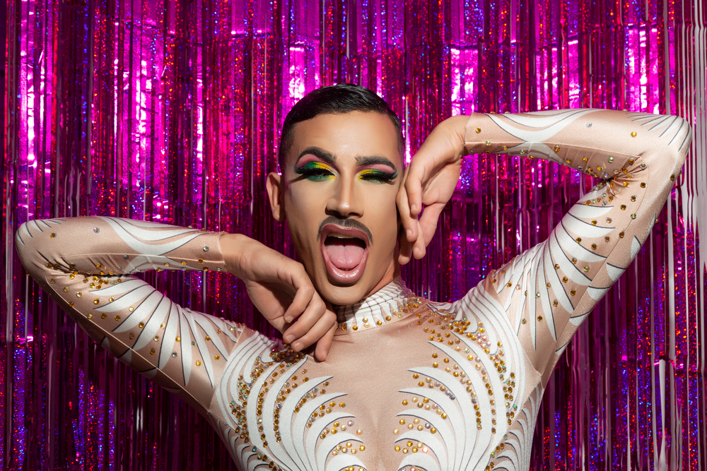 A performer in a white beaded bodysuit posing in front of a pink tinsel curtain