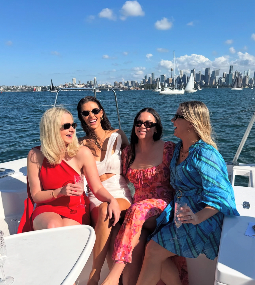Britt and three friends in bright dresses laughing together on deck, the city skyline across the water