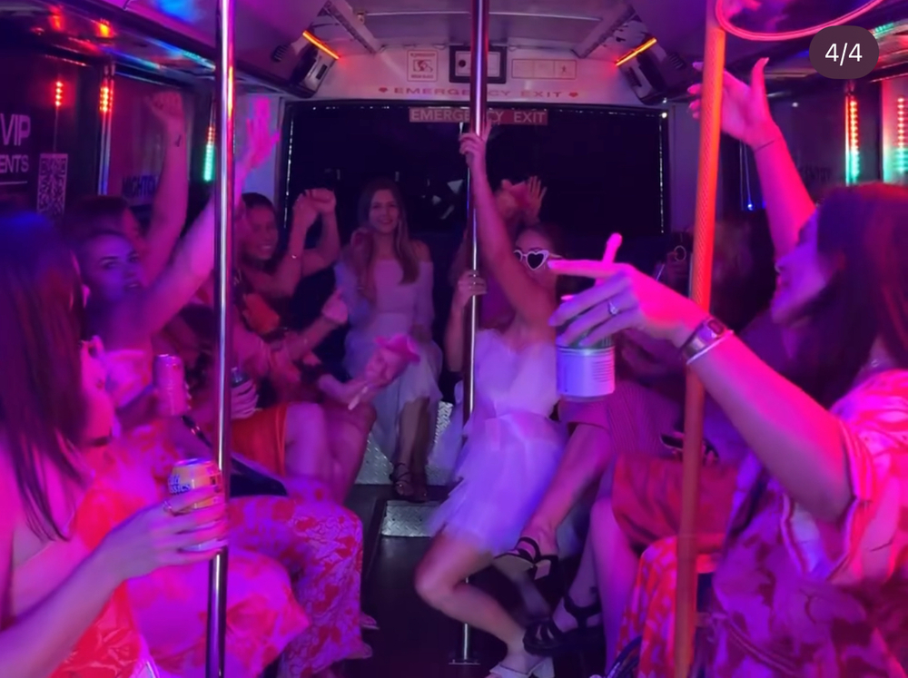 A hens group singing and dancing in a pink-lit party bus