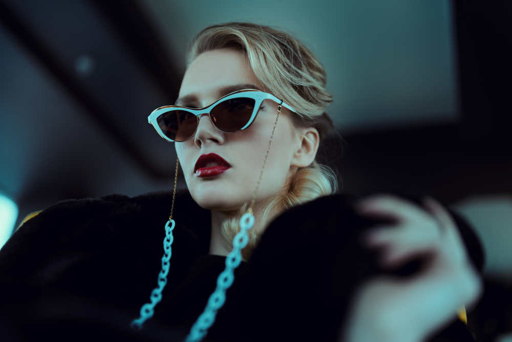 A woman in cat-eye sunglasses with a jewelled chain and a black fur collar