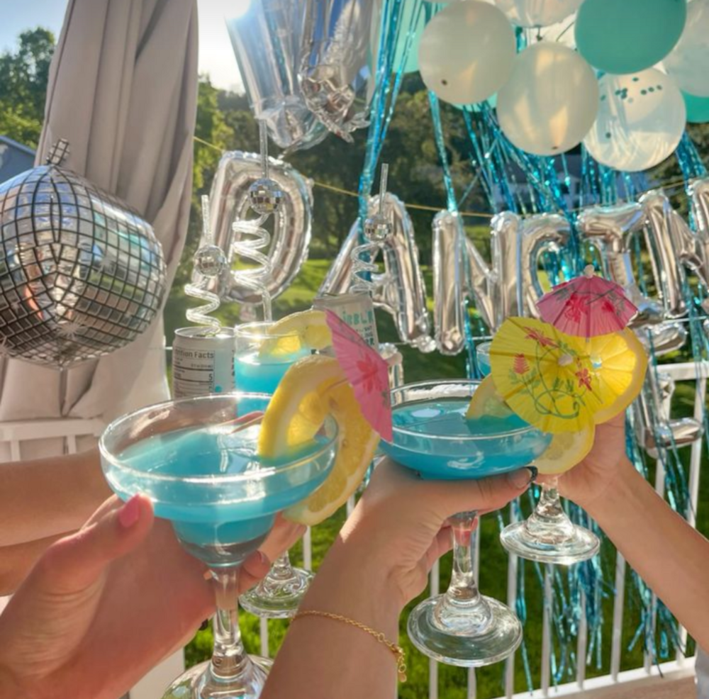 Blue cocktails raised in front of silver balloons and a mirror ball