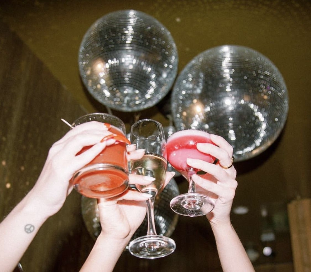 Two hands clinking pink cocktails under a pair of mirror balls