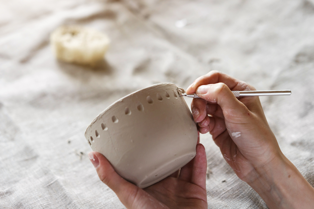 Hands carving a pattern into a small clay bowl