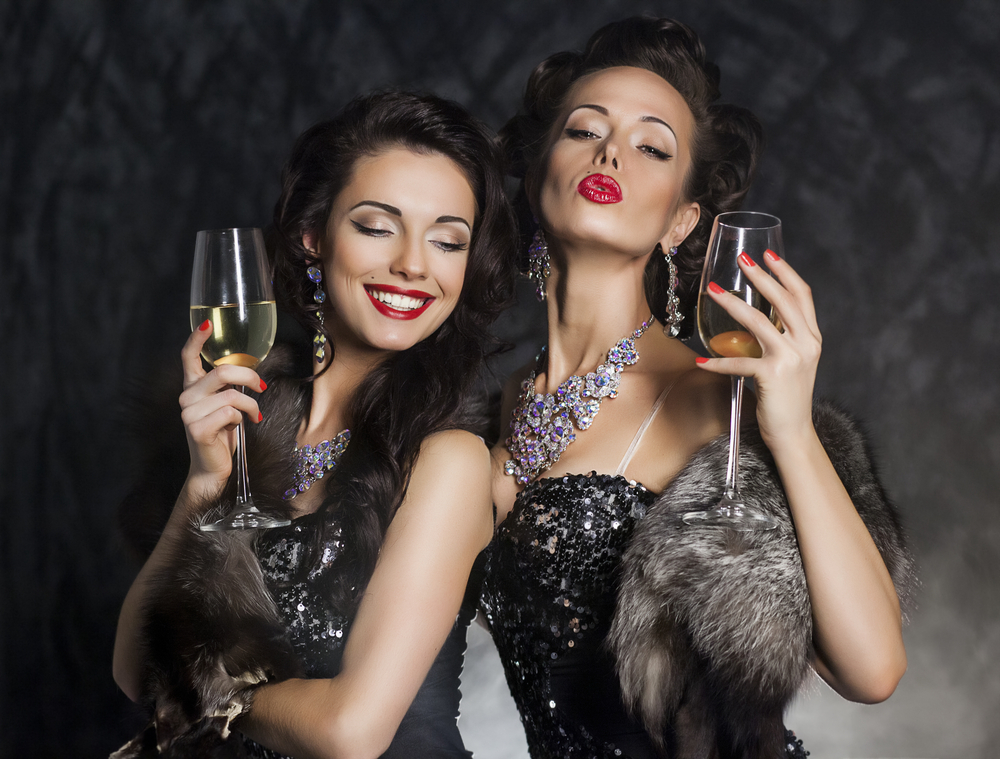 Two women in fur and dark lipstick holding glasses of champagne