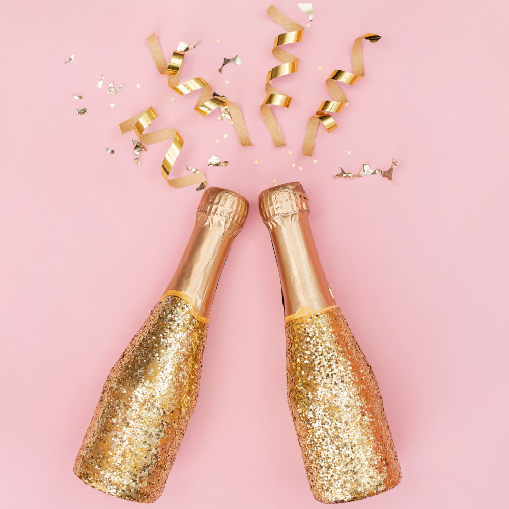 Two gold glitter bottles of bubbly with gold streamers on a pink background