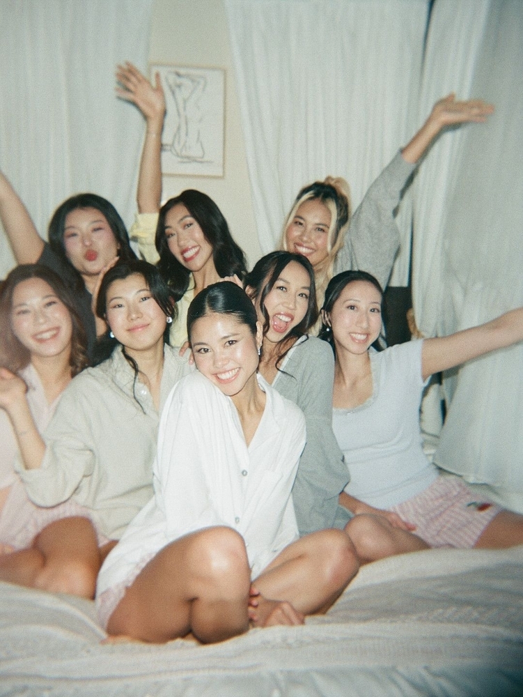 A group of friends in pyjamas cheering together on a bed