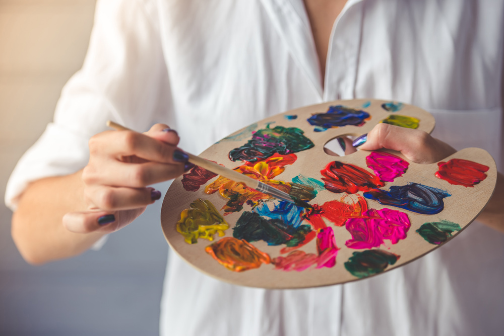 Hands holding a paint palette loaded with bright colours