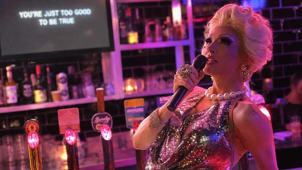 One of our drag queens in sequins and pearls, singing into the microphone at the bar