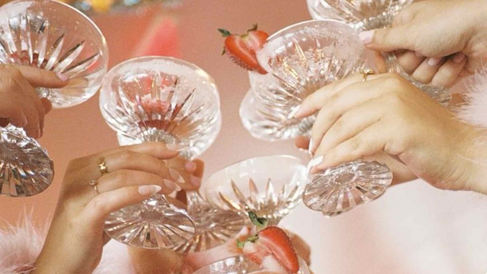 Hands clinking crystal coupe glasses of pink bubbles with strawberries