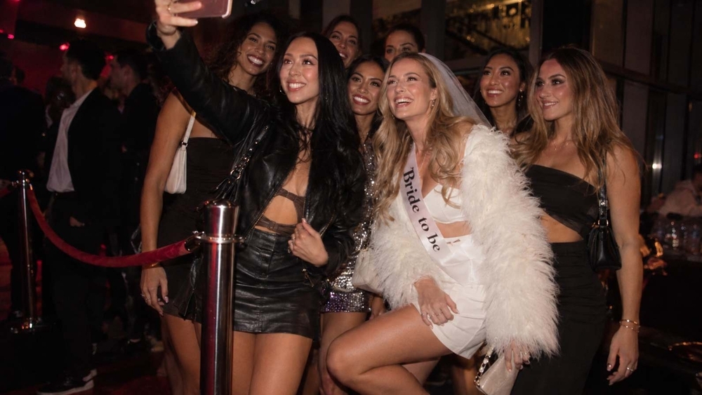 The bride in a white jacket and sash with her crew at a nightclub