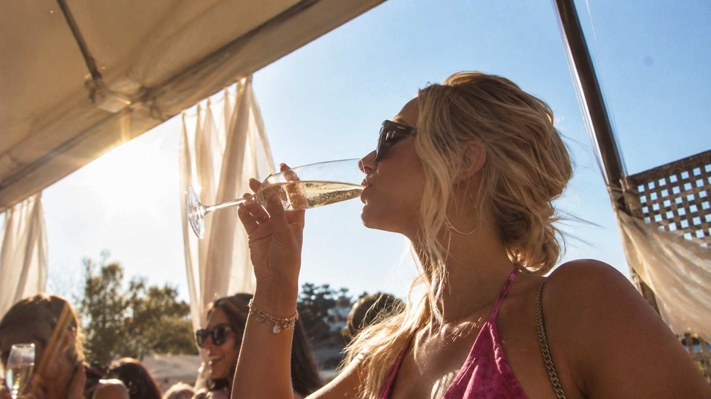A woman in sunglasses sipping bubbles under the awning of a boat on a sunny afternoon