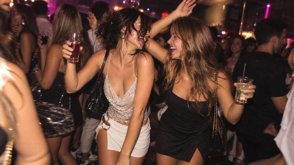 Friends dancing with drinks in the air on a crowded dance floor