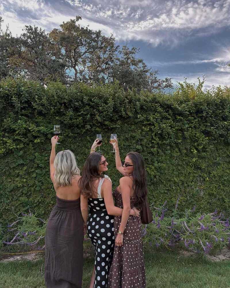 Three friends raising their glasses in a garden, seen from behind
