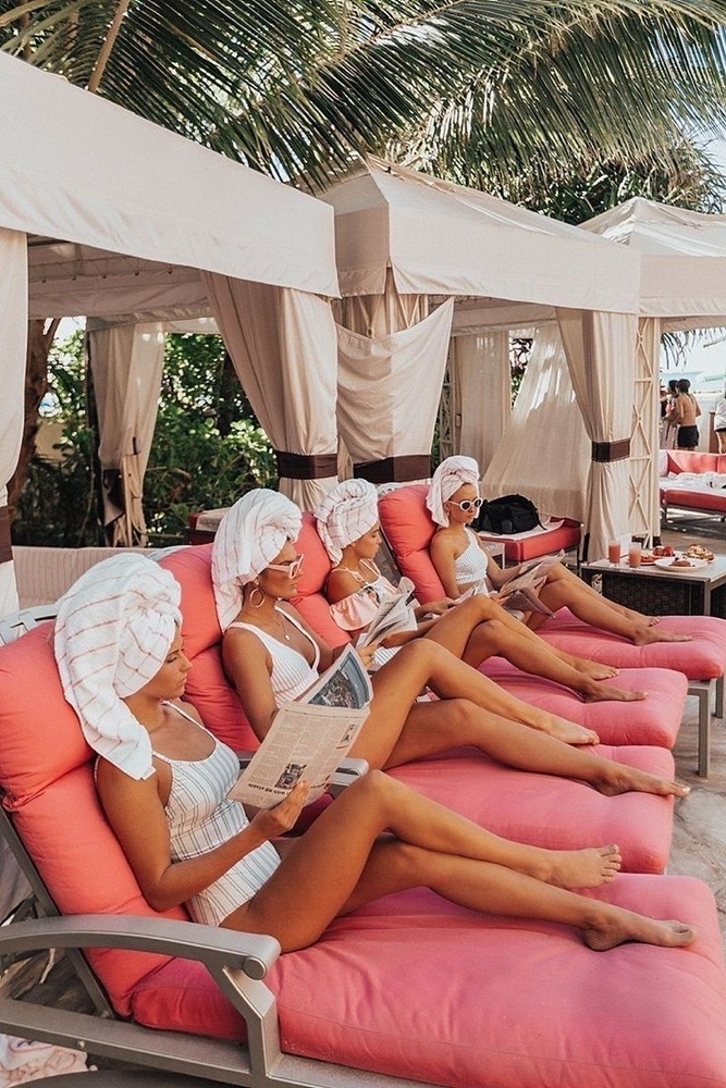 Women in towel turbans lounging on pink poolside daybeds
