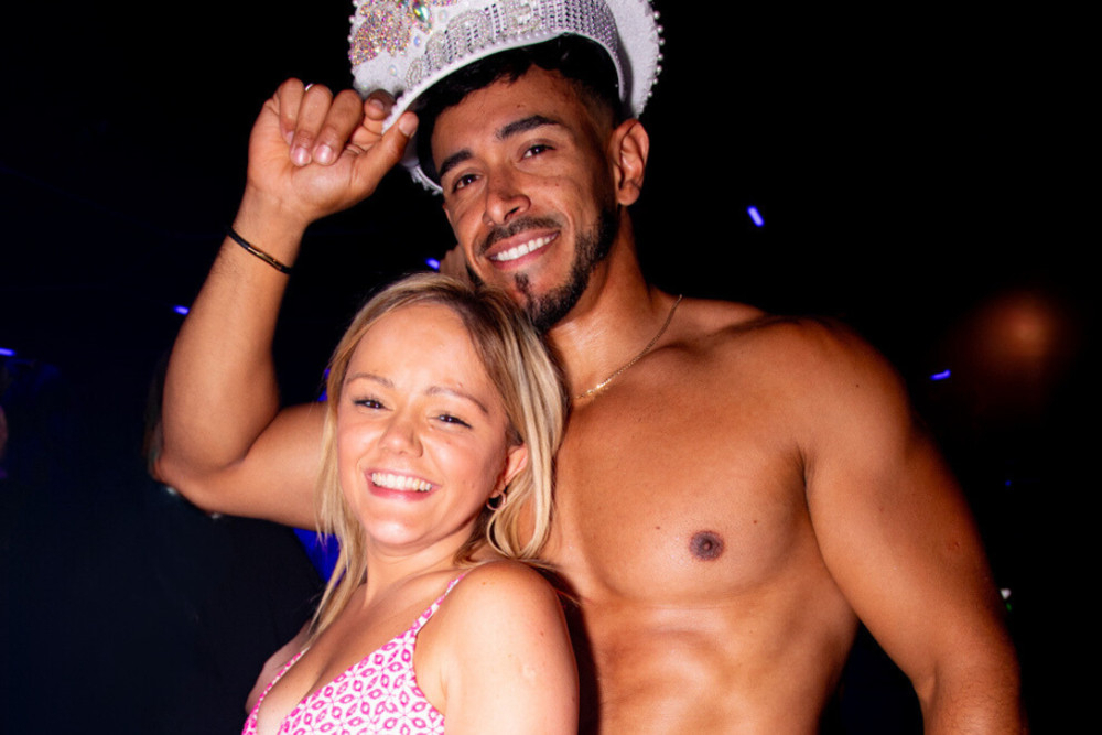A shirtless waiter in a sparkly bride hat poses with a smiling hen