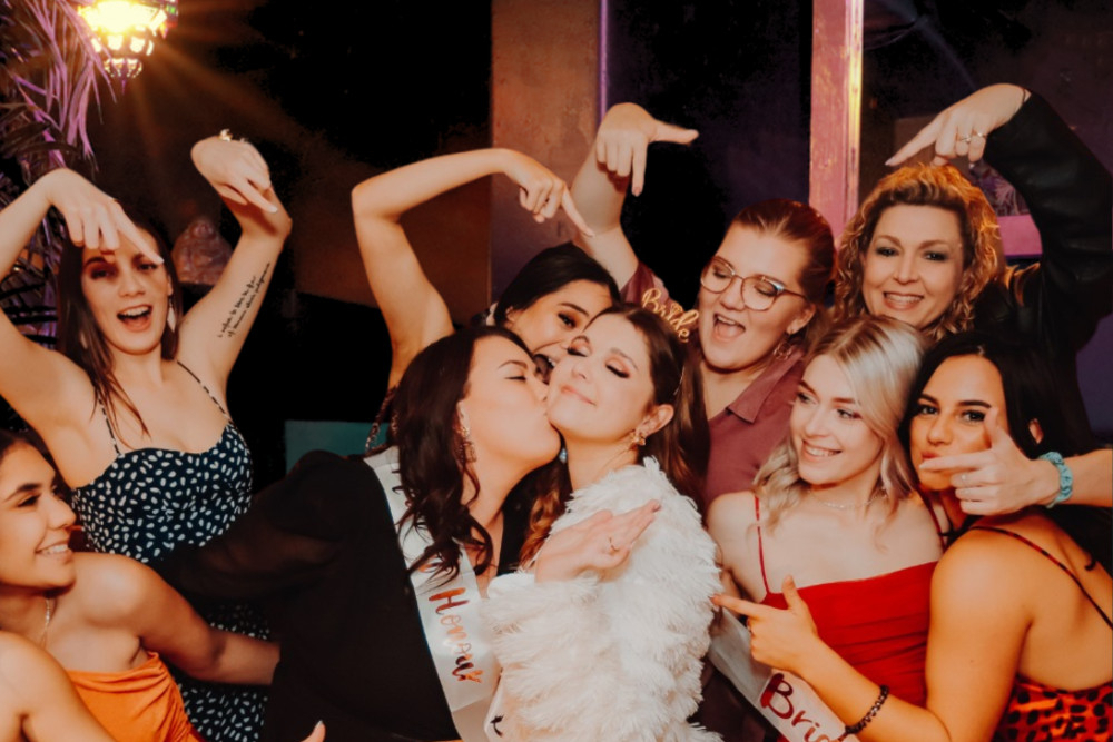 Hens dancing and pointing at the bride in a white fluffy jacket