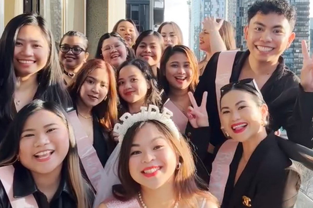 A hens crew in sashes gathered around the bride in her veil on a city balcony