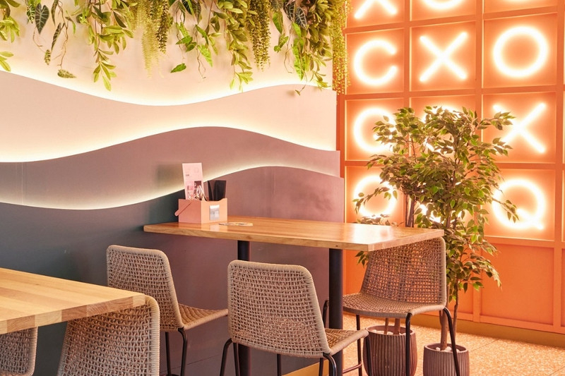 A cocktail bar room with a pink neon letter wall, hanging greenery and high tables