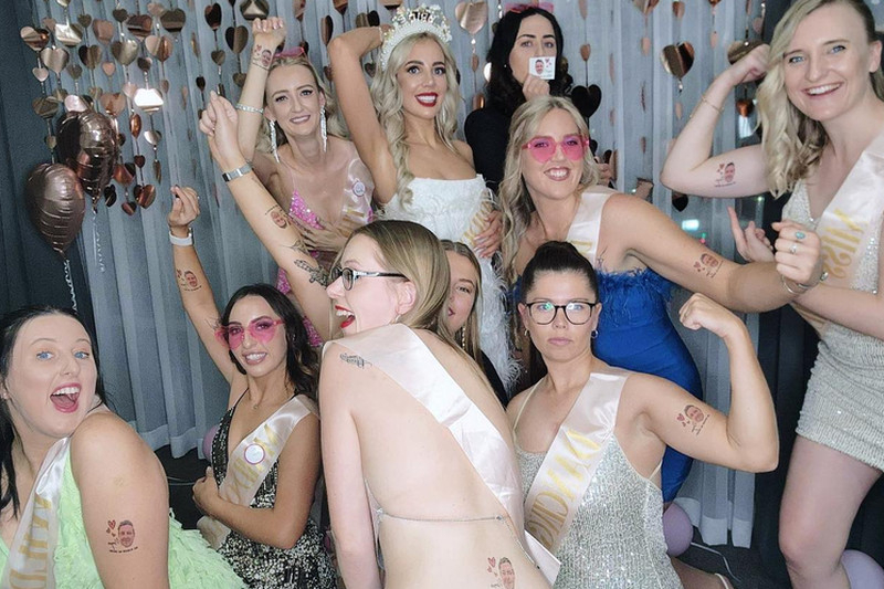 Friends in sashes flexing and posing around the bride in her tiara at a hens dance class