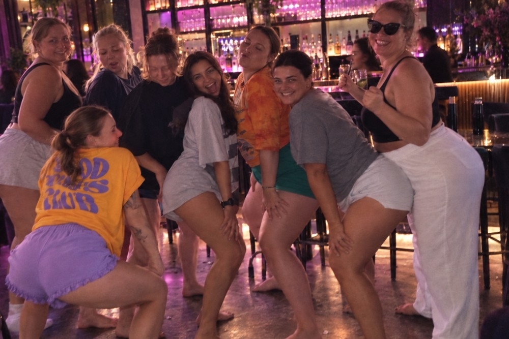 Friends in comfy shorts and tees laughing their way through a dance routine in a lounge