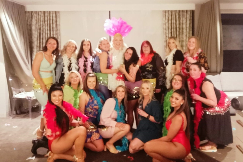A hens crew in colourful feather boas posing together after their dance class in a bright function room