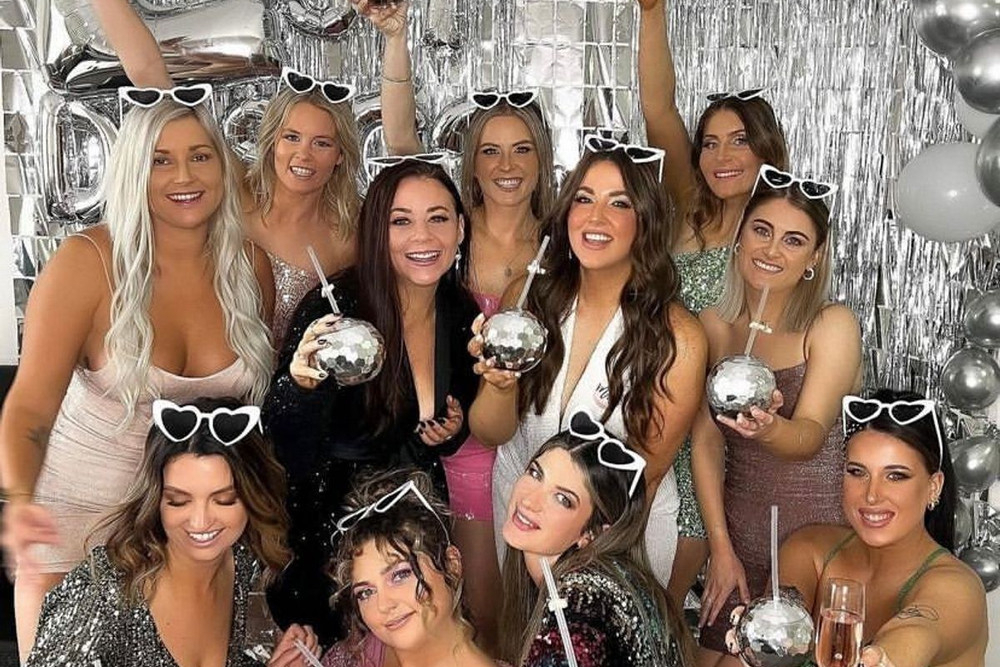 A hens group in sequins holding disco ball cups in front of a silver wall