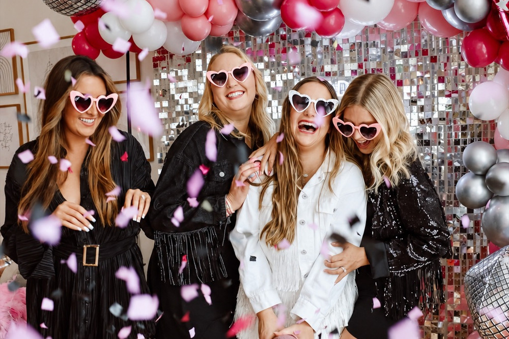 A hens crew in heart sunglasses dancing as confetti falls in front of a disco backdrop