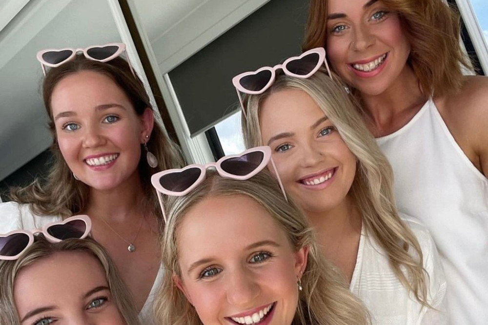 Five friends in heart-shaped sunglasses squeezing into a laughing selfie