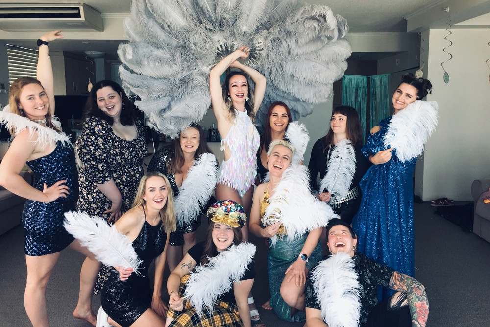 A hens crew posing with big white feather fans after their burlesque class