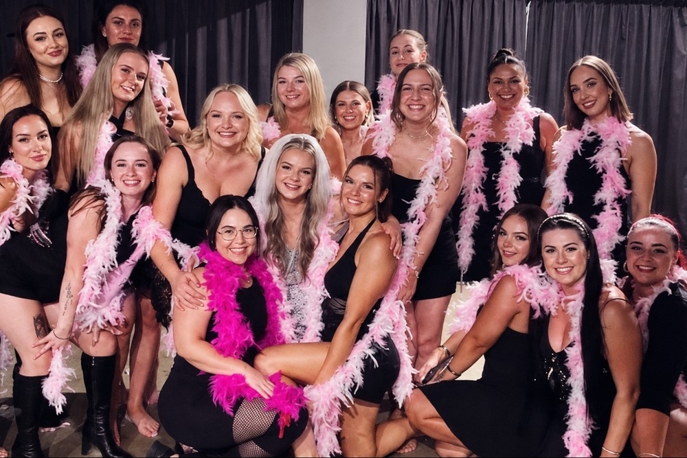 A big hens group in black dresses and pink feather boas after their burlesque class