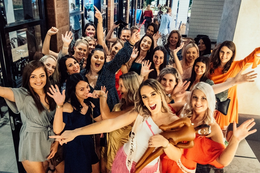 A big crew of friends cheering with their arms out at a bar