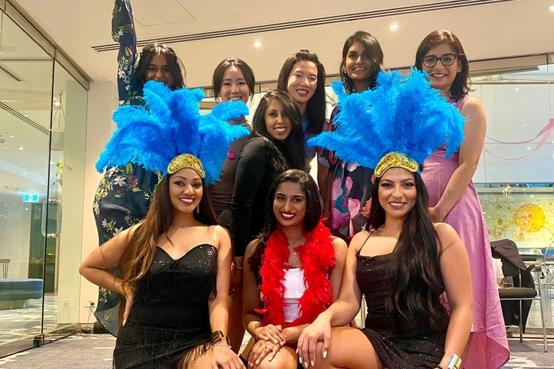 A hens group with blue feather headdresses and a red boa posing together after their burlesque class