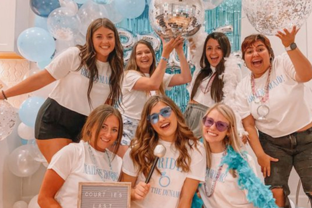 A hens group in matching white tees with disco balls and blue balloons at a Mamma Mia hens night