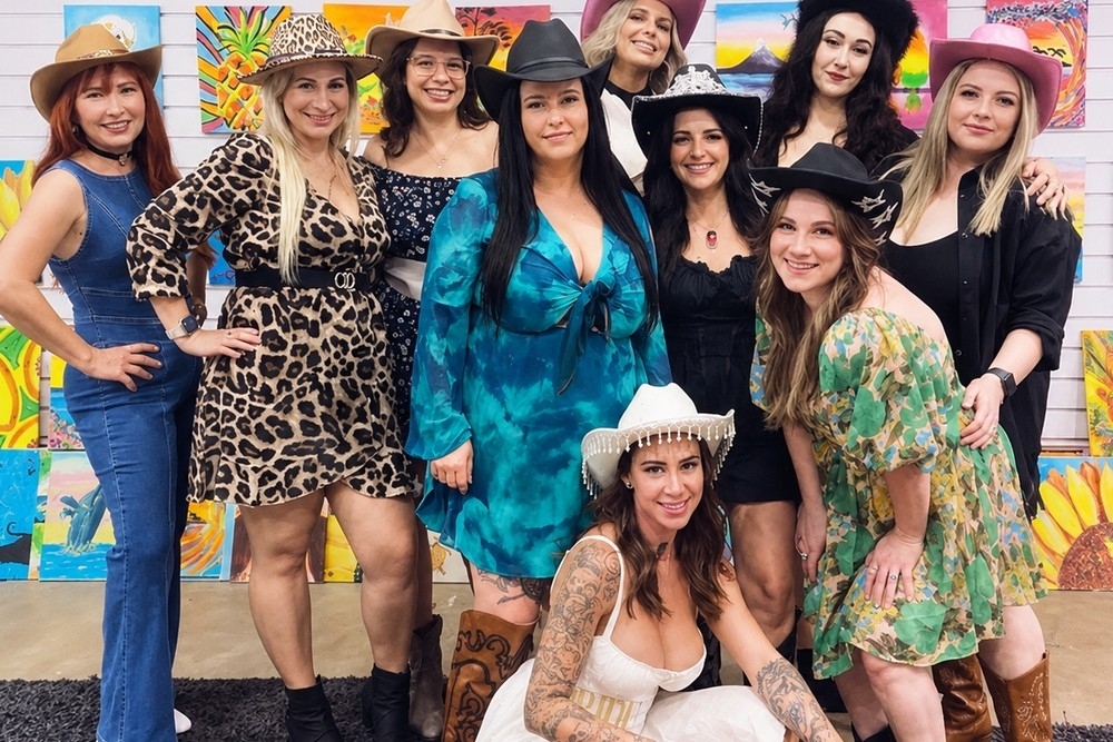 Friends in leopard print, denim, florals and black with cowboy hats and boots posing in front of a wall of bright painted canvases